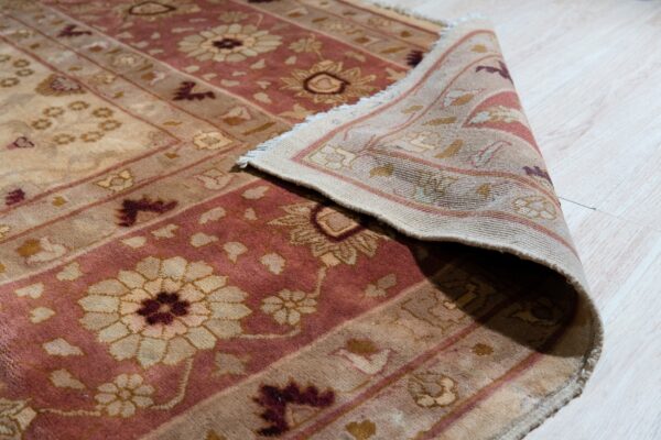 A high-pile beige and dusty rose rug with a floral pattern is rolled back on light wood flooring.