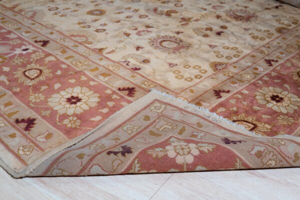 Traditional floral rug in beige and pink colors, with a corner folded over light wood floor.