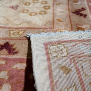 Close-up of a beige and maroon patterned rug folded to reveal the woven backing and fringe.