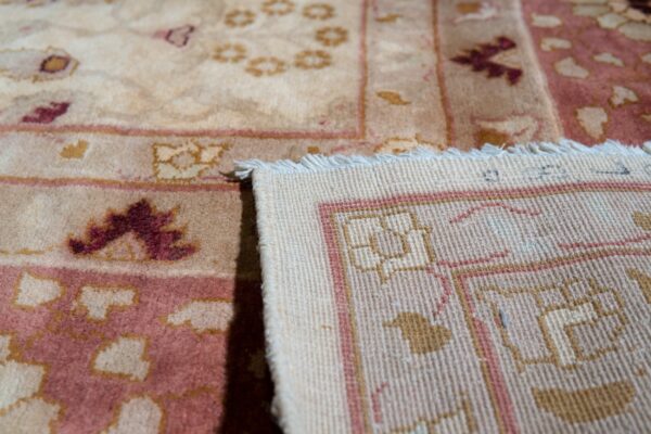 Close-up of a beige and maroon patterned rug folded to reveal the woven backing and fringe.