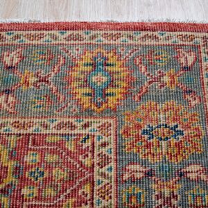 Detail shot of a tightly woven low-pile rug featuring red, gray, yellow, and blue traditional patterns on light wood flooring.