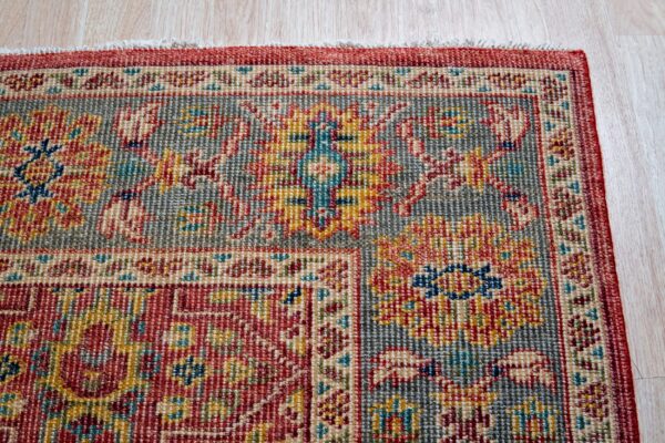 Detail shot of a tightly woven low-pile rug featuring red, gray, yellow, and blue traditional patterns on light wood flooring.