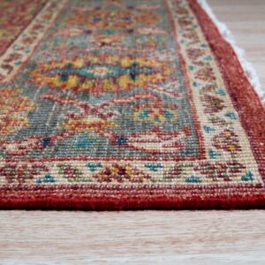 Low-angle detail of a short-pile rug with red, gray, and yellow traditional patterns on light wood floors.