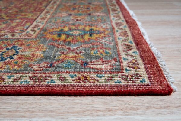 Low-angle detail of a short-pile rug with red, gray, and yellow traditional patterns on light wood floors.
