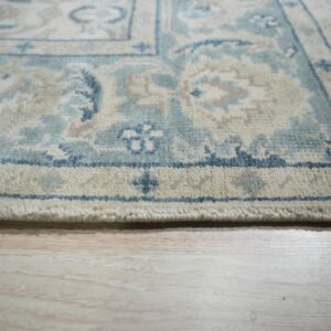 Thick-pile rug with blue, cream, and taupe traditional patterns resting on light wood floor.