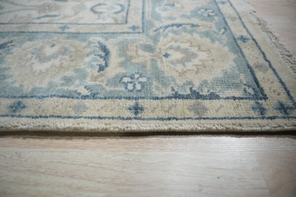 Thick-pile rug with blue, cream, and taupe traditional patterns resting on light wood floor.