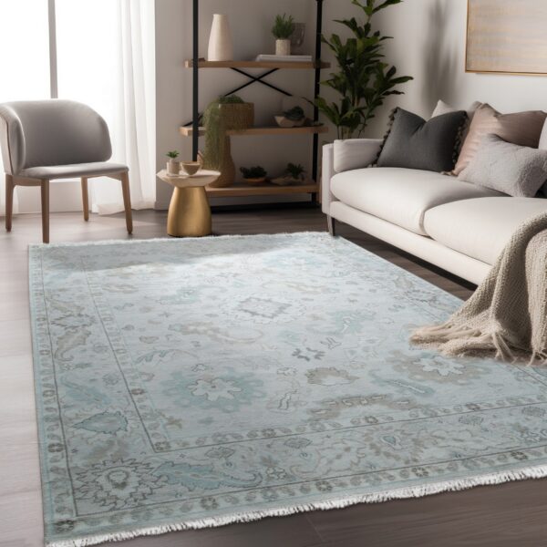 Light blue and taupe ornate rug with fringe sits on dark wood floors beside a white couch.