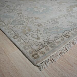 Muted floral rug in cream, tan, and light blue with visible fringe rests on blonde wood floor.