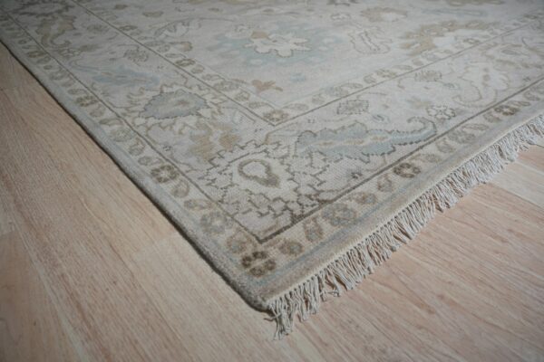 Muted floral rug in cream, tan, and light blue with visible fringe rests on blonde wood floor.