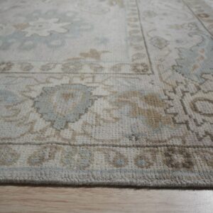Cream rug with traditional light blue and tan floral patterns viewed close up on light wood floor.