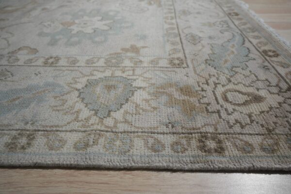 Cream rug with traditional light blue and tan floral patterns viewed close up on light wood floor.
