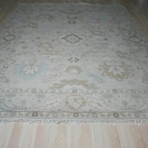 Traditional ivory rug with pale blue and beige floral patterns and fringe on a light wood floor.