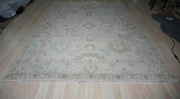 Traditional ivory rug with pale blue and beige floral patterns and fringe on a light wood floor.