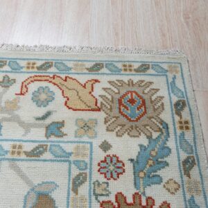 Ivory low-pile rug displaying blue, orange, and taupe traditional designs on pale wood floors.