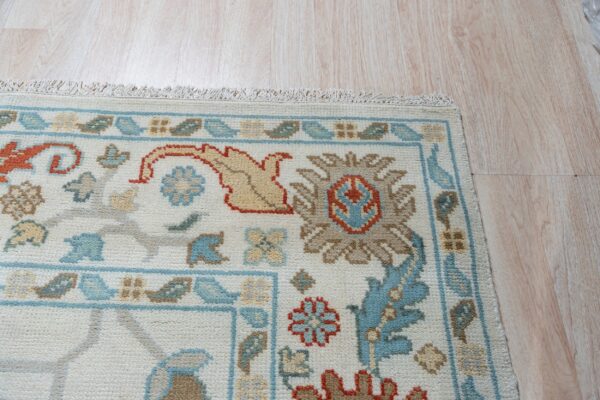 Ivory low-pile rug displaying blue, orange, and taupe traditional designs on pale wood floors.