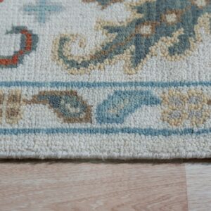 Detailed view of a textured cream rug with teal, orange, and tan ornate patterns on light wood flooring.