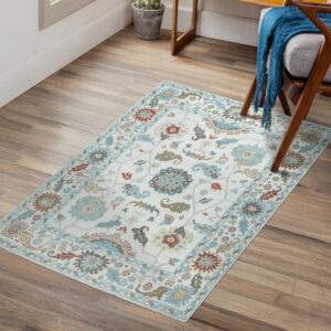 Cream rug with light blue and rust traditional motifs rests on wood floors near a wooden chair.