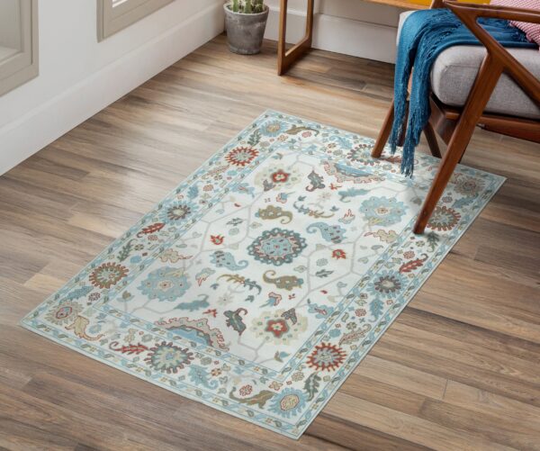 Cream rug with light blue and rust traditional motifs rests on wood floors near a wooden chair.