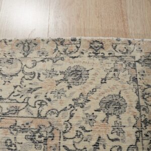 Distressed cream rug with black and peach traditional motifs lies on reflective light wood flooring.
