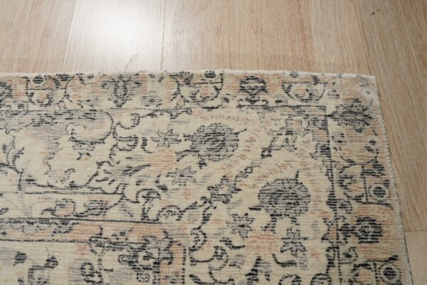 Distressed cream rug with black and peach traditional motifs lies on reflective light wood flooring.