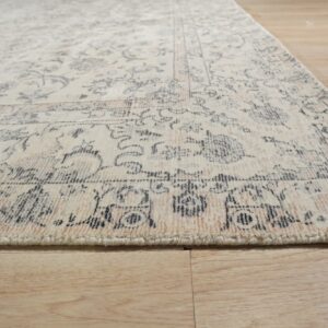 Plush cream rug with faded rose and charcoal traditional patterns lies on light wood flooring.