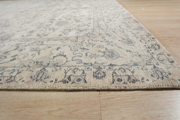 Plush cream rug with faded rose and charcoal traditional patterns lies on light wood flooring.