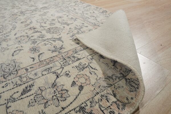 Distressed cream and dark gray patterned rug is rolled back, revealing the woven backing on light wood flooring.