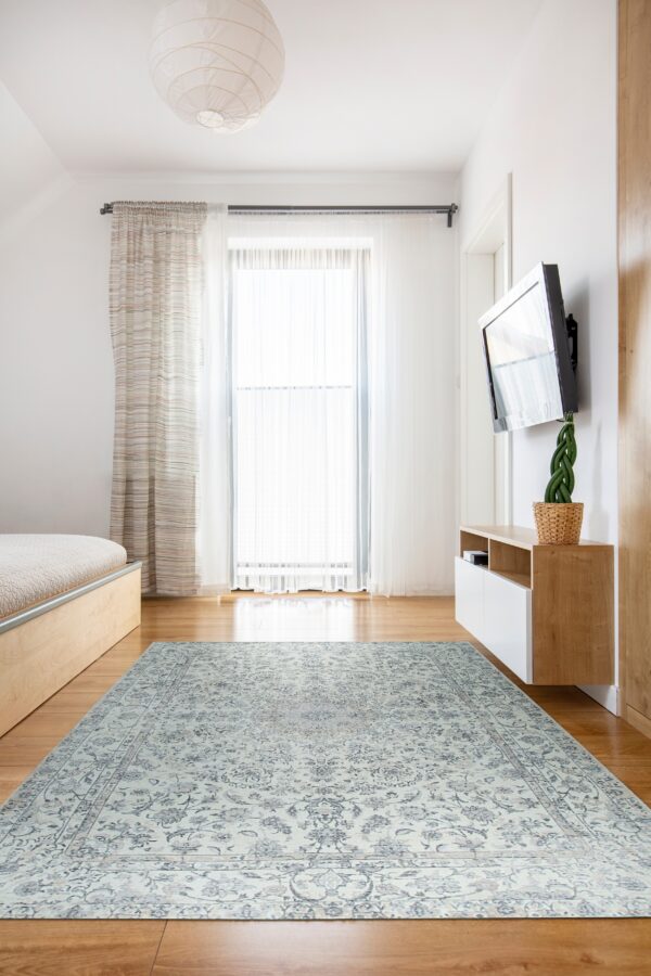A distressed pale blue and white traditional rug covers a wood floor in a brightly lit modern bedroom.