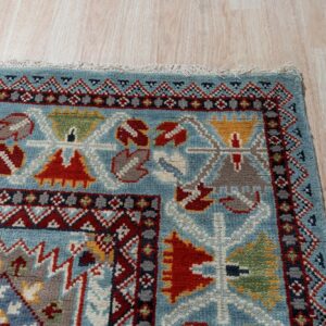 Close-up showing a thick pile blue rug with complex red and yellow geometric borders on light wood flooring.