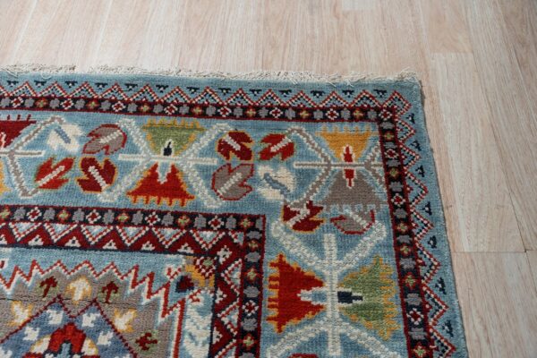 Close-up showing a thick pile blue rug with complex red and yellow geometric borders on light wood flooring.