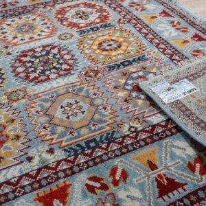 Close-up of a blue, red, and yellow geometric rug partially unrolled on light wood flooring.