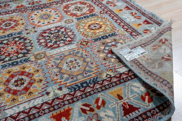 Close-up of a blue, red, and yellow geometric rug partially unrolled on light wood flooring.