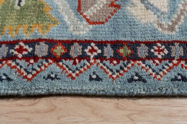 A textured blue rug close-up displays geometric red, navy, green, and yellow patterns on light wood floor.