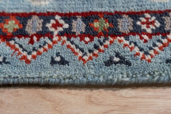 Detail of a medium-pile rug featuring blue, red, and navy geometric patterns on a light wooden surface.