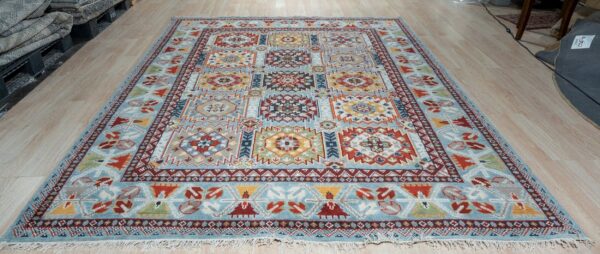 Blue rug featuring a multicolored geometric pattern of square medallions and visible fringes on wood flooring.
