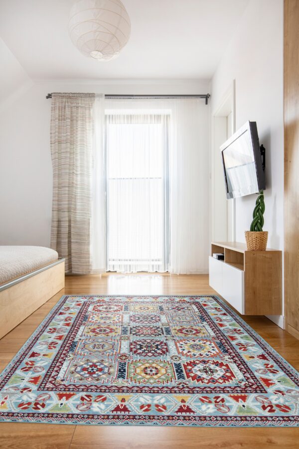 Geometric pale blue and multi-color area rug on a wood floor beneath a large window and tv.