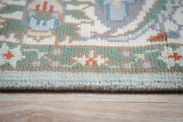 Pastel rug border with green, cream, lavender, and orange pattern rests on light wood planks.