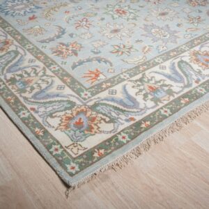 A pale blue floral rug with complex off-white and green borders rests on light wood flooring.