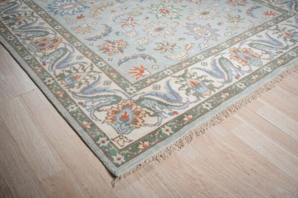 A pale blue floral rug with complex off-white and green borders rests on light wood flooring.