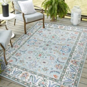 Outdoor light blue rug with a floral pattern rests beneath two cushioned patio chairs.