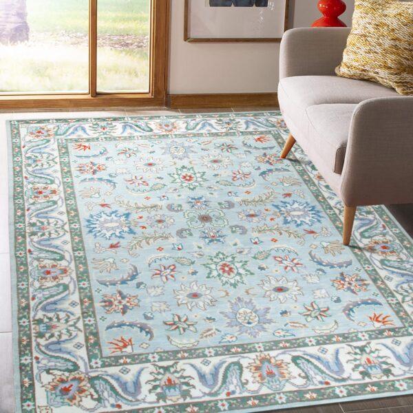 Light blue low-pile rug with colorful floral motifs next to a gray armchair by a window.