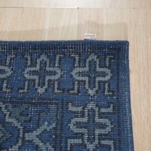 Navy and light blue geometric rug corner detail shows a textured pile on light wood planks.