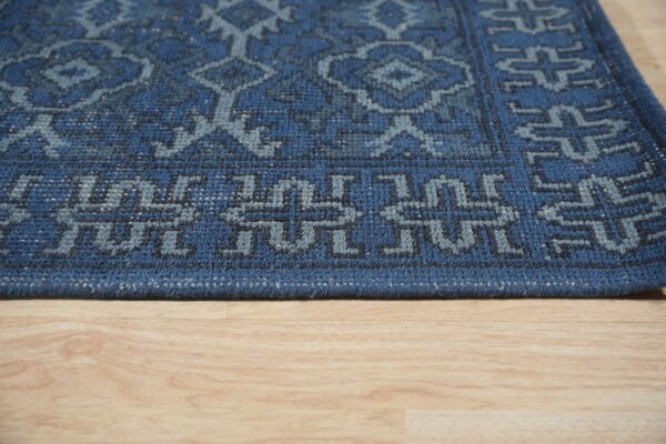 Close-up of a textured dark blue rug with light blue geometric patterns on wood flooring.