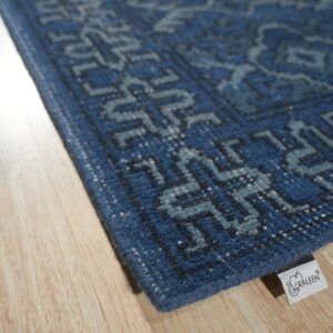 Angled view of a low-pile blue rug featuring light geometric patterns on light wooden floor planks.