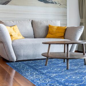 Royal blue patterned rug anchors a gray sofa with yellow pillows and a dark wooden coffee table.
