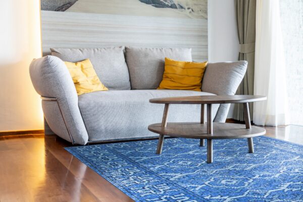 Royal blue patterned rug anchors a gray sofa with yellow pillows and a dark wooden coffee table.