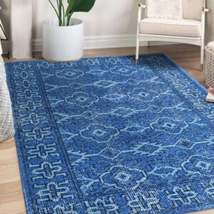 Blue distressed rug with geometric and medallion patterns lies on wood flooring beside a white chair.
