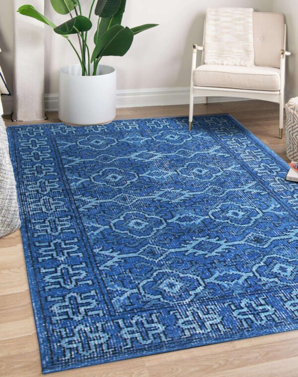 Blue distressed rug with geometric and medallion patterns lies on wood flooring beside a white chair.