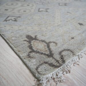 Textured beige rug with brown abstract motifs and fringe lays across light blonde flooring.