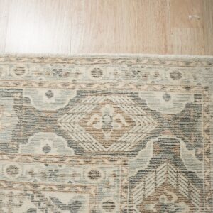 Distressed cream, blue, brown, and gray patterned rug corner on light wood plank flooring.